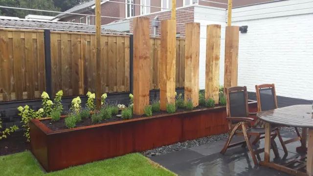 Verhoogde border van cortenstaal bij een houten schutting en terras