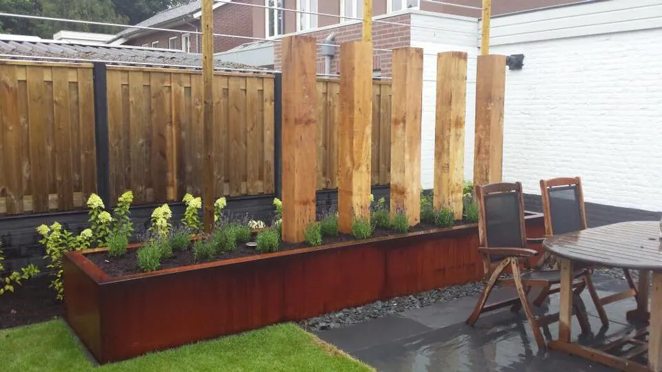 Verhoogde border van cortenstaal bij een houten schutting en terras